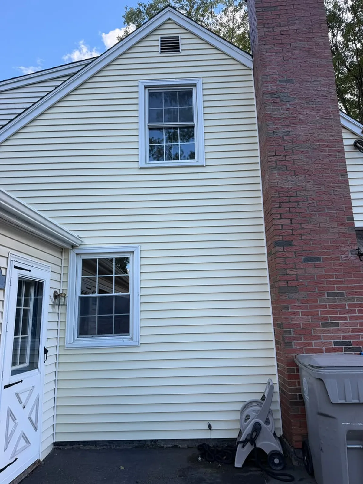 Cream vinyl siding gable with brick chimney close-up
